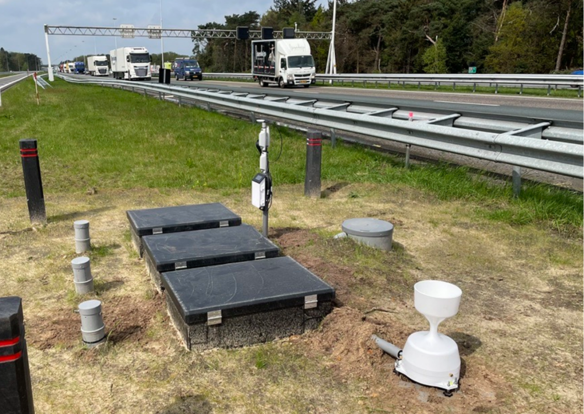 Meetopstelling van drie zwarte boxen en pijpen in de berm langs de snelweg